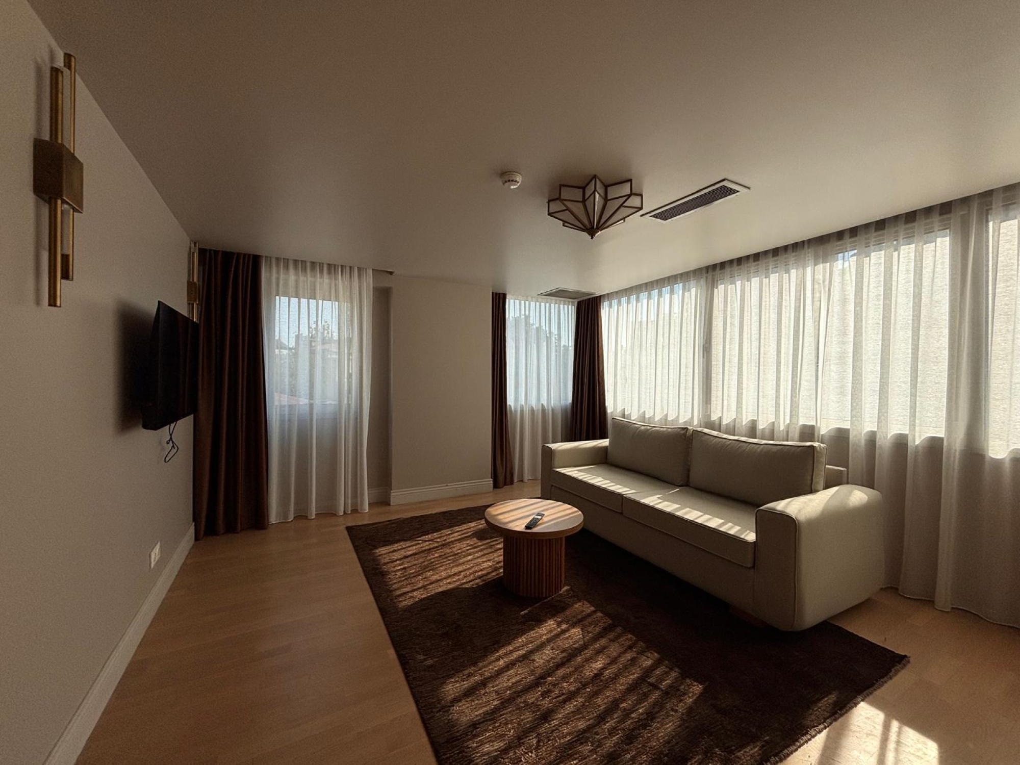 Living room with sofa beside curtained windows and a wall-mounted TV.