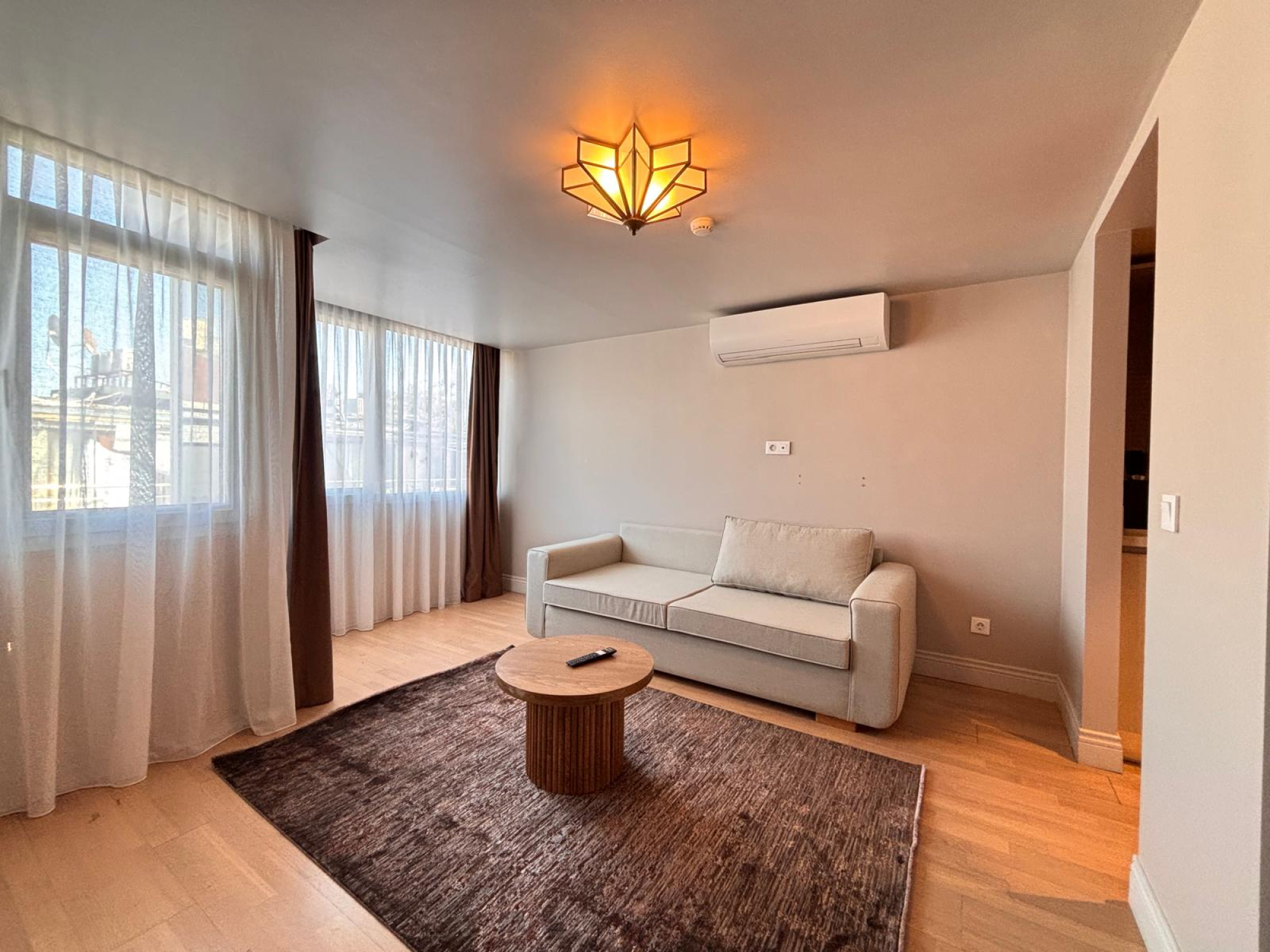 Bright living room with sofa, coffee table, air conditioning and wraparound windows.