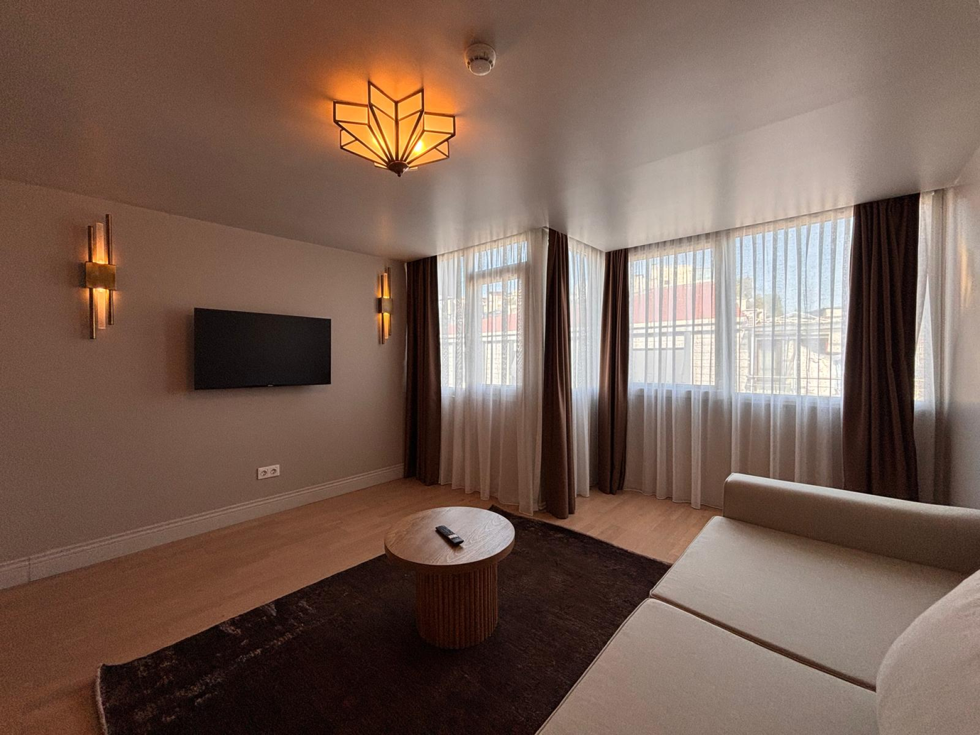 Living room with corner sofa, wall-mounted TV and full-height windows.