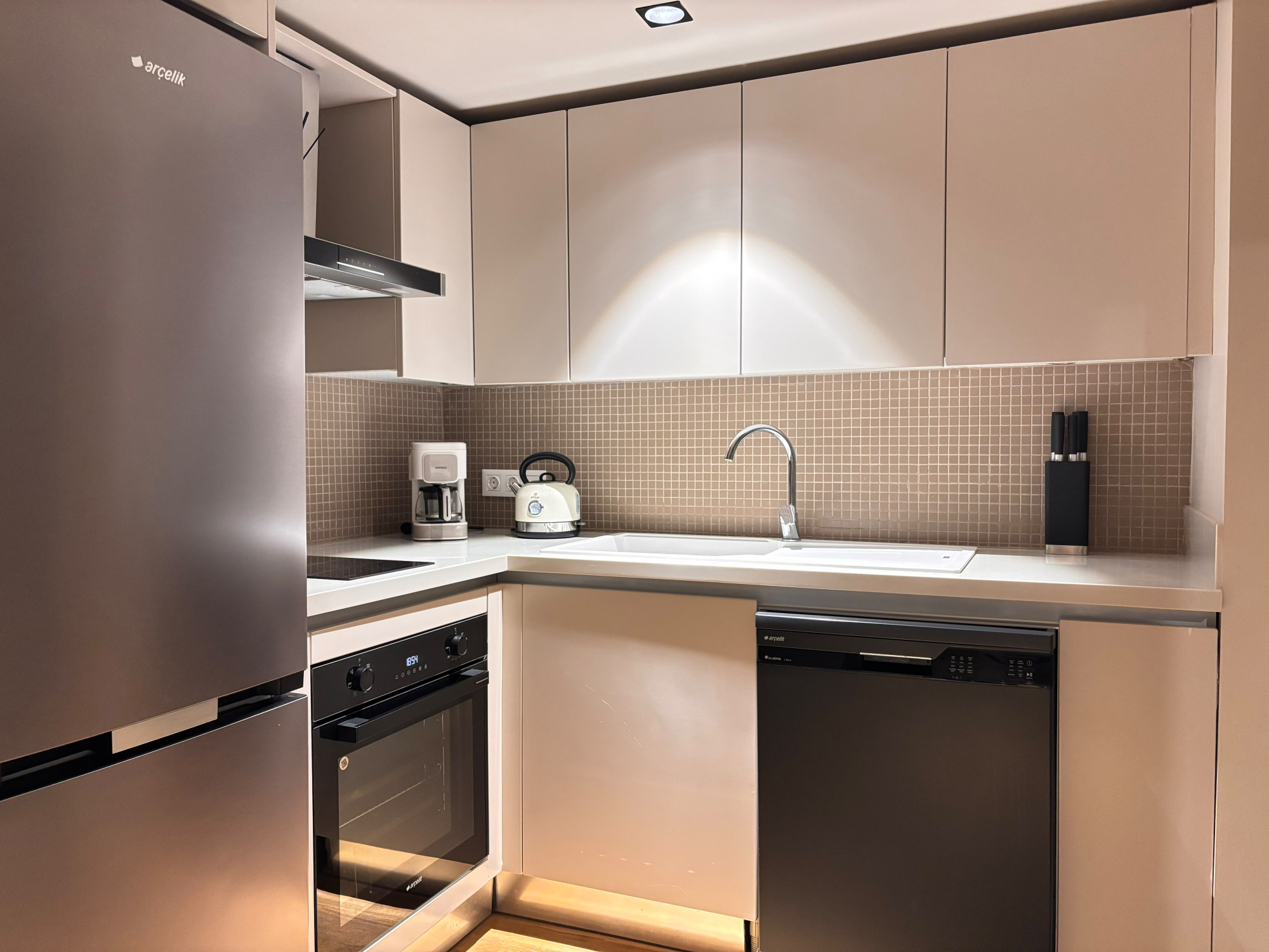 L-shaped kitchen with refrigerator, oven, cooktop, sink and cabinets.